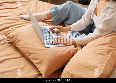 Remote work and digital nomad lifestyle, woman working on laptop in bed, comfortable home office setup Stock Photo