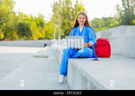 Medical education and online learning, young female doctor or student using laptop outdoors for remote study Stock Photo