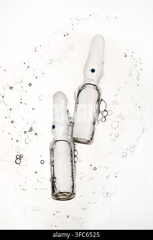 Two transparent glass ampoules floating in liquid with air bubbles Stock Photo