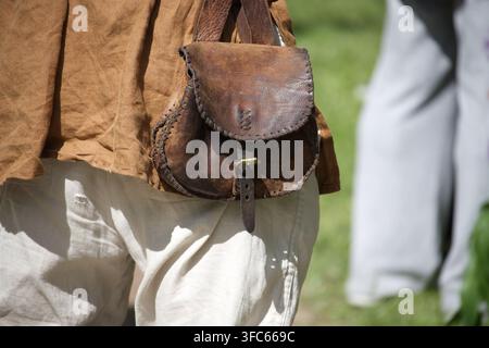 Close-up of a worn leather pouch hanging from the waist over linen trousers and a brown tunic, showing hand-stitched details and a rustic, historical Stock Photo