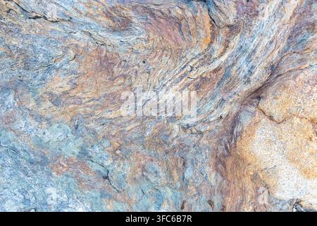 Macro shot of layered metamorphic stone texture showing rich brown and grey mineral veins in a natural wavy pattern, ideal for abstract wallpaper. Stock Photo