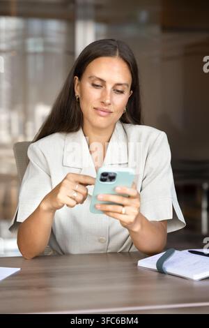 Focused businesswoman sitting at desk using smartphone to check messages Stock Photo