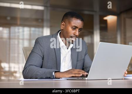 Black businessman sitting at office desk typing on laptop Stock Photo