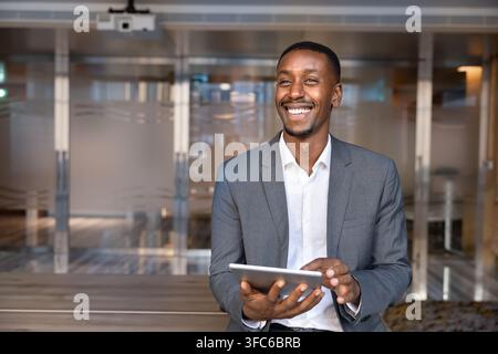 Smiling African businessman holding digital tablet in corporate office Stock Photo