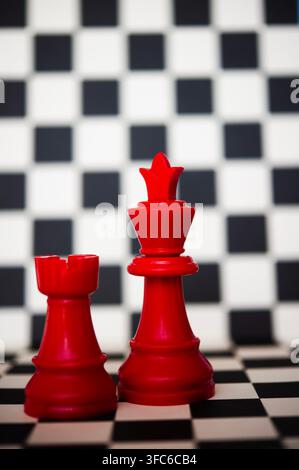 Red rook and king chess pieces standing together on a black and white chessboard, suggesting teamwork, alliance, strategy and power Stock Photo