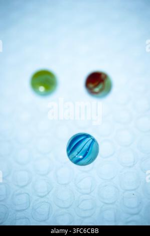 lue glass marble in sharp focus with green and red marbles blurred behind on a pale blue textured surface, creating a playful abstract still life Stock Photo