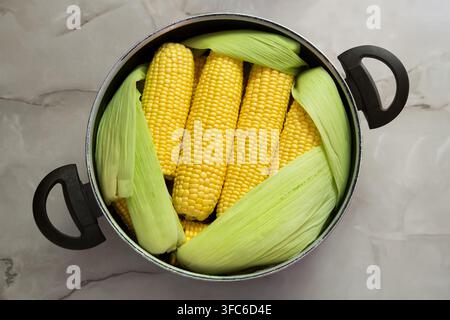 Corn in a saucepan on the table. Fresh corn prepared for cooking. View from above. Stock Photo