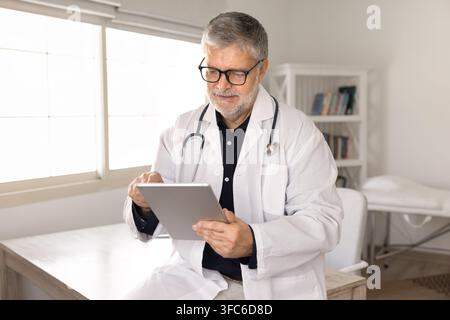 Senior doctor checking patient data on digital tablet in clinic Stock Photo