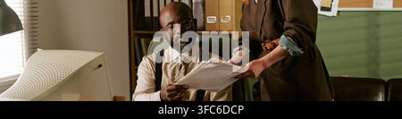 Header of Black Middle Aged Manager Reviewing Paper Documents in Retro Office Stock Photo