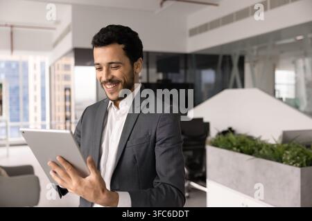 Smiling Middle-eastern businessman working on digital tablet in corporate office Stock Photo