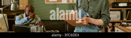 Header of Woman Writing on Clipboard with Black Man Repairing Pc in Retro Office Stock Photo