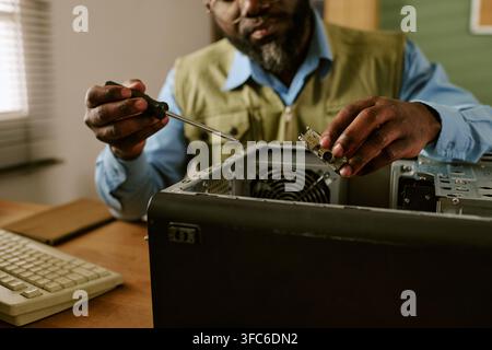Black Man Repairing Retro Computer with Screwdriver in Office Stock Photo