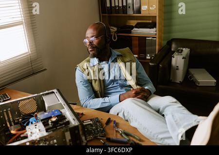 Black Man Repairing Computer in Retro Office Looking out Window Stock Photo