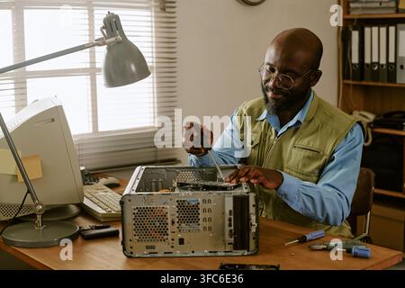 Black Middle Aged Technician Fixing Vintage Computer in Retro Office Stock Photo