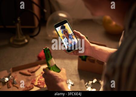 Man Having Video Call with Black Woman on Smartphone at Party Stock Photo