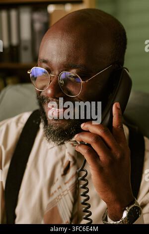 Smiling Black Middle Aged Man Talking on Retro Telephone in Office Stock Photo