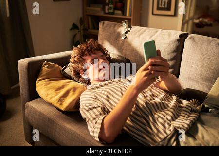 Man Lying on Sofa and Using Smartphone for Social Media Browsing Stock Photo