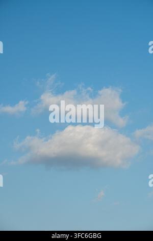 Fluffy white clouds, floating in the bright blue sky. The clouds are described as resembling soft cotton and are often used as a backdrop. Stock Photo