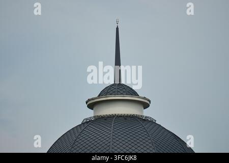 Low angle close up shot of a dark steel building spire and textured tiled dome against a flat overcast Stock Photo