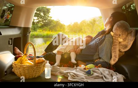 Baby sleeping peacefully in mother's arms during car camping Stock Photo