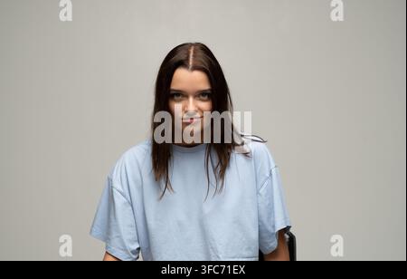 Confident brunette woman giving a subtle smirk, looking powerful and self-assured in studio portrait, expressing determination Stock Photo