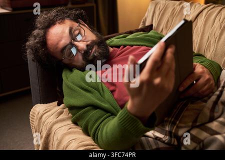 Middle Aged Man Lying on Sofa and Using Digital Tablet at Home Stock Photo