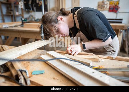 Passionate woman crafter at work in restoration workshop, working with wooden material at table Stock Photo