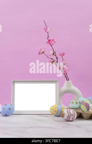 A delightful decor with an empty frame, cherry blossoms and colorful Easter eggs against a pink background Stock Photo
