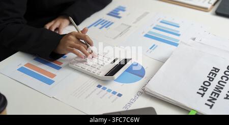 A professional accountant calculates expenses using a calculator surrounded by financial reports and graphics. The focus is on budgeting Stock Photo