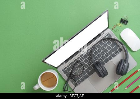 A laptop with headphones, glasses, and stationery on a green background, symbolizing modern learning or remote work Stock Photo