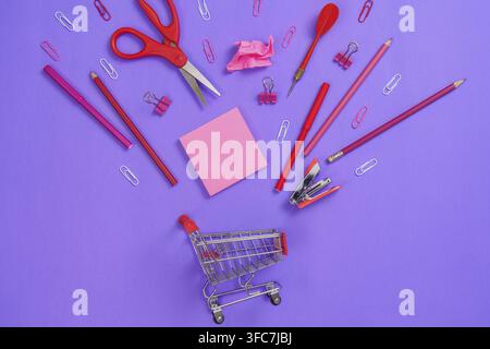 An arrangement of red school supplies, including scissors, pens, and paper clips, creatively presented on a purple background Stock Photo