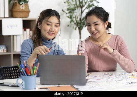 Two designers who collaborate on UX and UI projects and share ideas and sketches while working on a laptop in a modern work area Stock Photo
