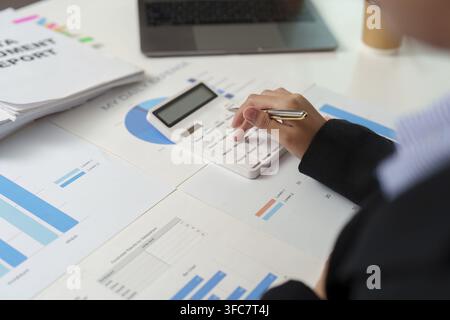 An accountant uses a calculator to analyze financial data, surrounded by reports and charts. Focus on budgeting and cost tracking Stock Photo