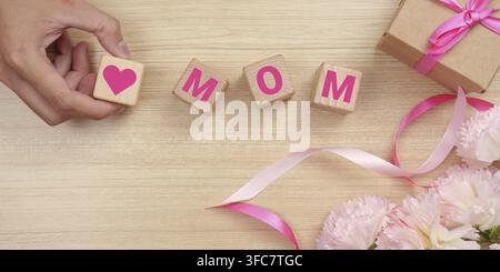 A creative arrangement with wooden blocks with the words "Mama", a wrapped gift and pink flowers that symbolize love and celebration Stock Photo