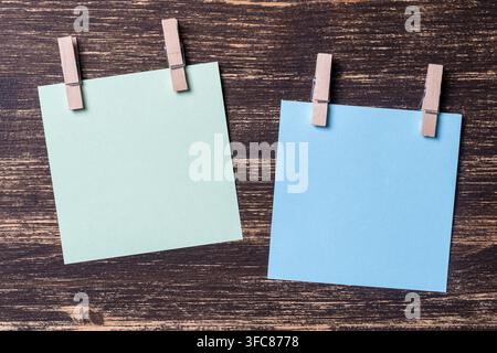 Empty colored paper sheets for notes with clothespins on wooden background. Blank cards on mockup template. Wooden clothespins with sheets of paper. B Stock Photo