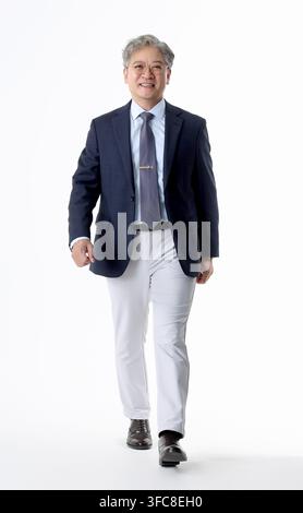 Confident senior Korean executive walking forward in formal business attire against a white background. Stock Photo