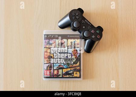 GTA V game with a Playstation controller. Grand Theft Auto 5 from Rockstar Games lying on a table. Close-up of the videogame cover in the case. Stock Photo