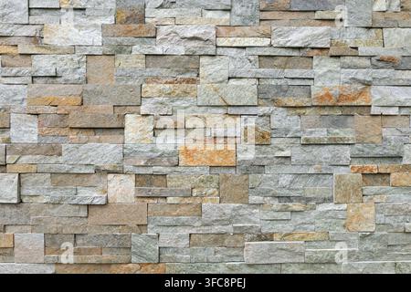 Stone cladding wall made of striped stacked bricks of natural multicolor rocks. External wall covering, background and texture. Stock Photo