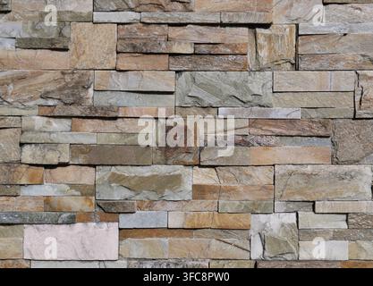 Multicolored external wall made of different types of rocks with different shapes. Background and texture. Stock Photo