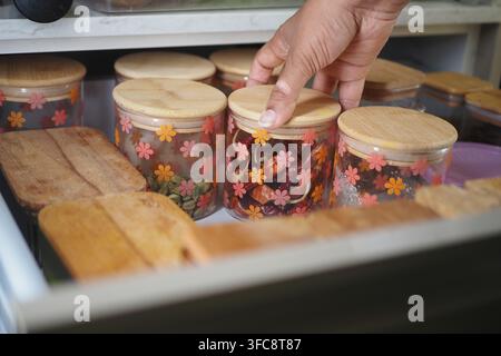 A hand is placing a lid on a jar in a kitchen. Various jars are arranged. Stock Photo