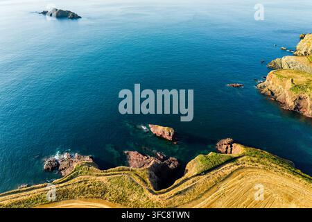 Elevated view of coastal cliff top with winding walking trail, rocky outcrops and reefs visible through turquoise shallows beside deep ocean water Stock Photo