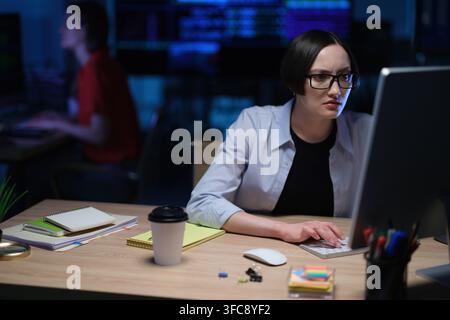 Tired woman office worker works late at night in quiet office Stock Photo