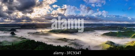Aerial view of rolling green hills blanketed in morning mist with dramatic sunbeams breaking through clouds over the landscape in Tarata, Taranaki Reg Stock Photo