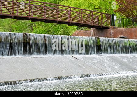 Smooth milky waters plunge over a man-made waterfall with a steel bridge above the flowing cascade on a spring day in Missouri. Stock Photo