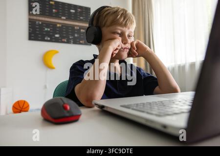 Boy with headphones using laptop computer at home in his room. Learning, homeworks, movie watching Stock Photo