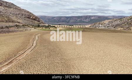 Aerial view of the arid landscape of the Little Karoo with a dam wall in the distance, featuring cracked earth and dry terrain in Garden Route Distric Stock Photo