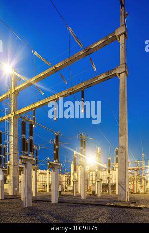 An illuminated electrical substation featuring high voltage equipment, transformers, and concrete support structures at twilight in Brazil. Stock Photo