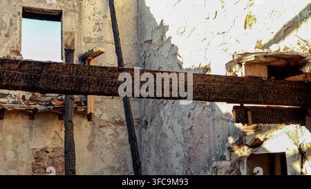 Detailed shot of heavily charred wooden structural beams against a weathered plaster wall in a fire-damaged building. Stock Photo