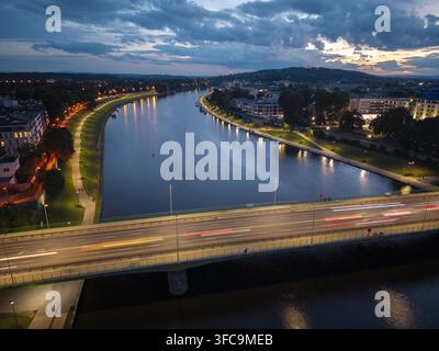 Aerial view of the Vistula River at night with light trails from traffic on the bridge, illuminated riverside paths, and city buildings in Krakow, Les Stock Photo