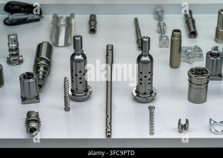 Assortment of high-precision CNC machined metal parts, threaded shafts, and turned stainless steel components on white display table Stock Photo